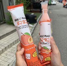 two people holding up orange juice and yogurt bars in front of a city street