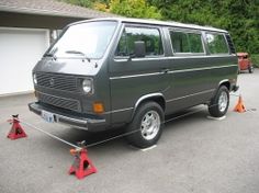 an old van is parked in a driveway with orange cones around it and trees behind it