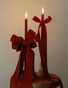 two lit candles are on top of a piece of wood that has been wrapped in red ribbon