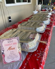 many pans are lined up on a long red table with a sign that says west family deli