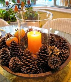 pine cones and oranges are arranged around a lit candle on a glass table with wicker chairs in the background