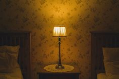 two beds side by side in a room with floral wallpaper and a lamp on the nightstand