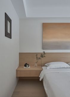 a bed with white sheets and pillows next to a painting on the wall above it