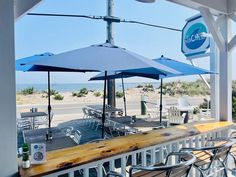 an outdoor restaurant with tables and umbrellas on the deck overlooking the beach in front of it