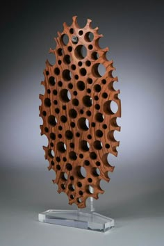 a sculpture made out of wood with holes in the center on a clear stand against a gray background