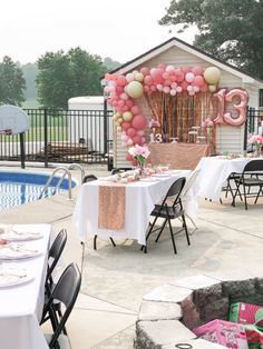 an outdoor party set up with balloons and table cloths near a swimming pool in the background