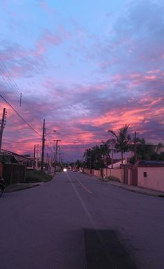 an empty street at dusk with the sun setting in the distance and palm trees on either side