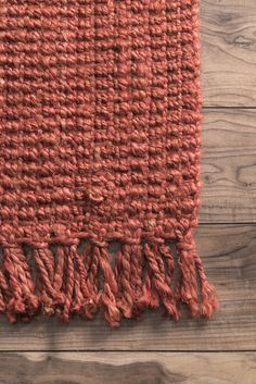 an orange rug with fringes on top of a wooden floor next to a wall