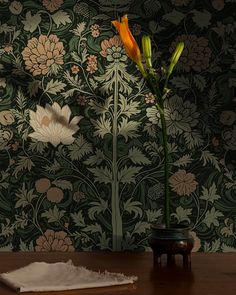 a flower in a vase sitting on a table next to a wallpapered wall