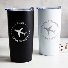 two travel mugs sitting next to each other on top of a white countertop