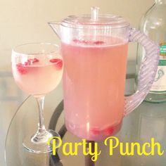 a drink in a pitcher next to a glass filled with pink liquid on a table