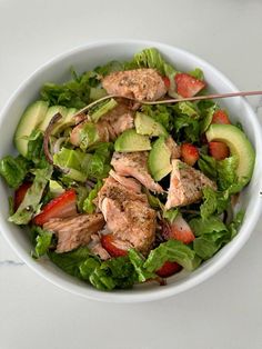 a white bowl filled with salad and meat on top of a table next to a fork