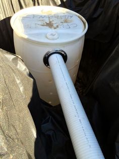 a white bucket with a hose attached to it sitting on top of a black tarp