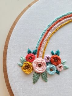 a close up of a embroidery on a hoop with flowers and rainbows in it