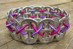 a close up of a metal bracelet on a wooden table with pink and purple cords