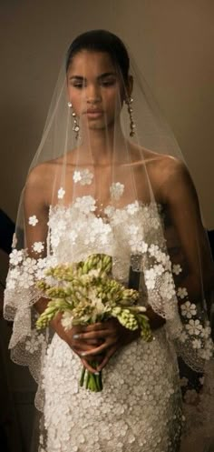 a woman in a white wedding dress holding a bouquet of flowers and wearing a veil