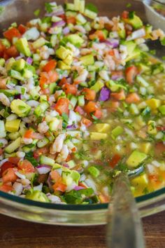 a bowl filled with lots of vegetables on top of a wooden table next to a spoon