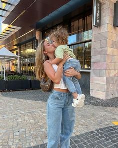 a woman holding a child in front of a building on a brick sidewalk with her face close to the ground