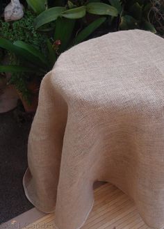 an elephant made out of burlap sitting on top of a wooden table next to potted plants