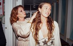 two women standing next to each other in front of a door and one is combing her hair