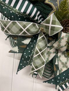 a green and white christmas wreath with pine cones, evergreens and plaid ribbon hanging on the front door