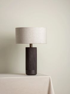 a table lamp sitting on top of a white cloth covered table next to a wall