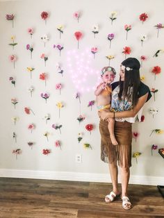 a woman holding a baby in front of a wall with flowers and hearts on it