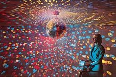 a man standing in front of a disco ball with lights coming from it and an image of a mirror ball floating above him