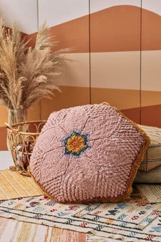 a pink cushion sitting on top of a rug next to a vase filled with dry grass