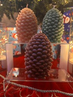 three pine cones sitting on top of a glass display case in front of a christmas tree