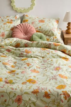 a bed with floral comforter and pillows on top of it, next to a night stand