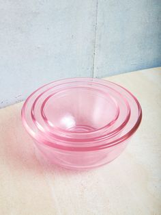 a pink glass bowl sitting on top of a wooden table next to a white wall