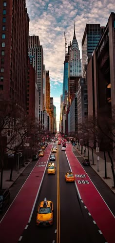 taxi cabs are driving down the street in new york city, with skyscrapers in the background