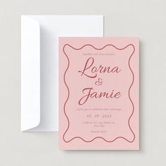 a pink wedding card with an ornate frame on the front and bottom, next to a white envelope