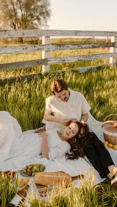 two women laying in the grass on a blanket near a basket of fruit and vegetables