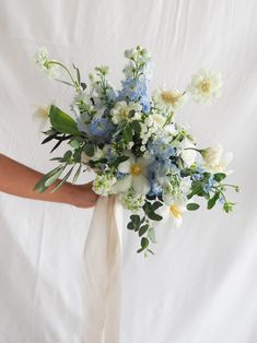 a bridal bouquet with blue and white flowers is held by someone's hand