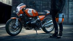 an orange and white motorcycle parked next to a person in black boots on the street