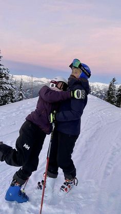 two people on skis hugging each other in the snow