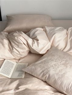 an open book laying on top of a bed covered in sheets and pillows, next to a pillow