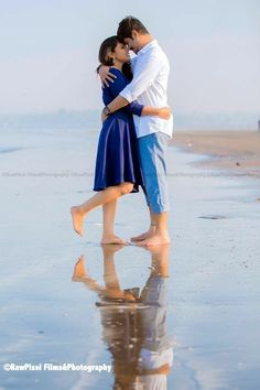 a man and woman kissing on the beach with their reflection in the wet sand as they stand close to each other