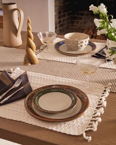 the table is set with plates, napkins and flowers in front of a fireplace