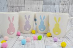 three coffee mugs decorated with bunny ears and pom - poms on a table