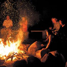 people sitting around a campfire at night with bright sparks coming from the fire pit