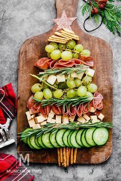 a wooden cutting board topped with cucumbers, cheese and crackers next to a christmas tree shaped platter