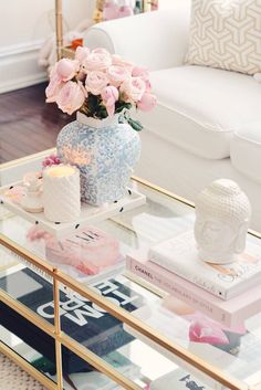 a glass table topped with pink flowers and books next to a white couch in a living room