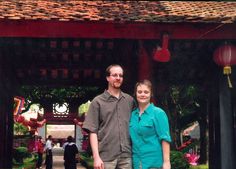 a man and woman are standing in front of a gazebo at a chinese garden