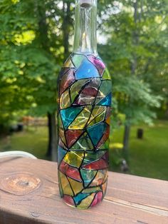 a glass bottle that is sitting on a wooden table with trees in the back ground