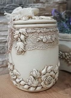 a white vase with flowers on it sitting on a table next to other pots and containers