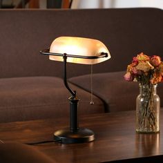 a table lamp sitting on top of a wooden table next to a vase with flowers