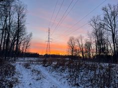 the sun is setting over a snowy field with power lines in the foreground and trees to the side